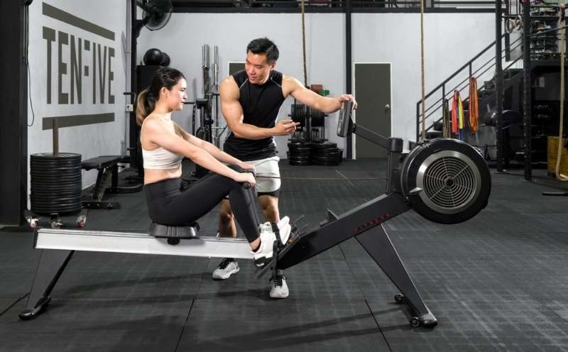 Trainer assisting a woman using a rowing machine in a gym, demonstrating guided fitness training.