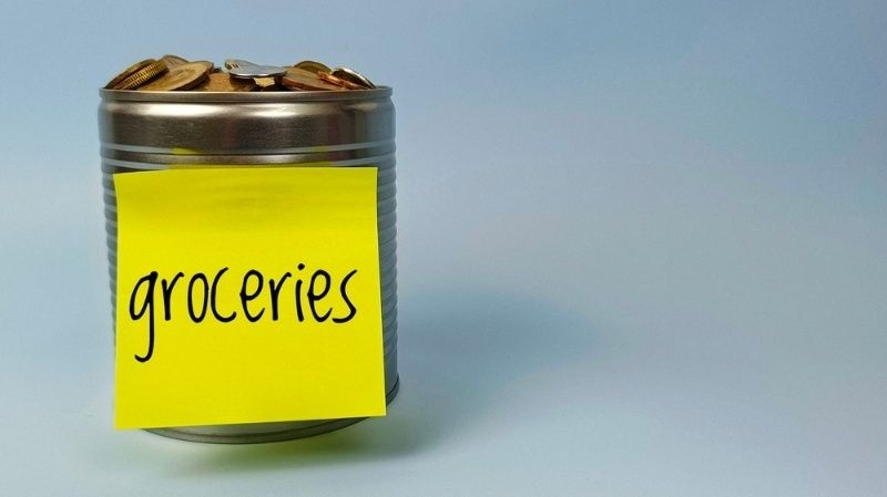 Tin can filled with coins labeled 'groceries' representing a grocery savings budget.