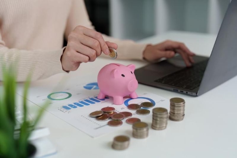 women putting coins in piggy bank on table