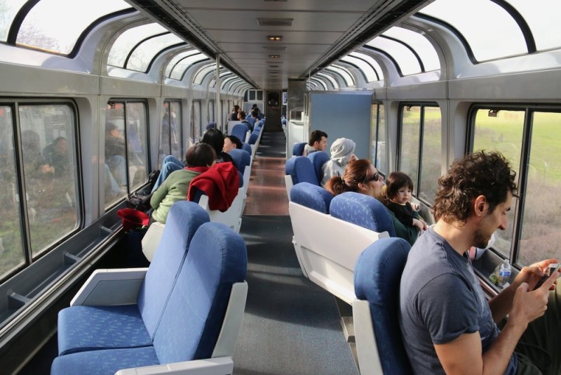 Passengers enjoying scenic views through large panoramic windows inside a sightseeing train car.