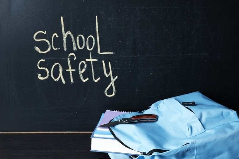 School safety concept showing a backpack and knife on a desk in front of a chalkboard with the words “School Safety.”