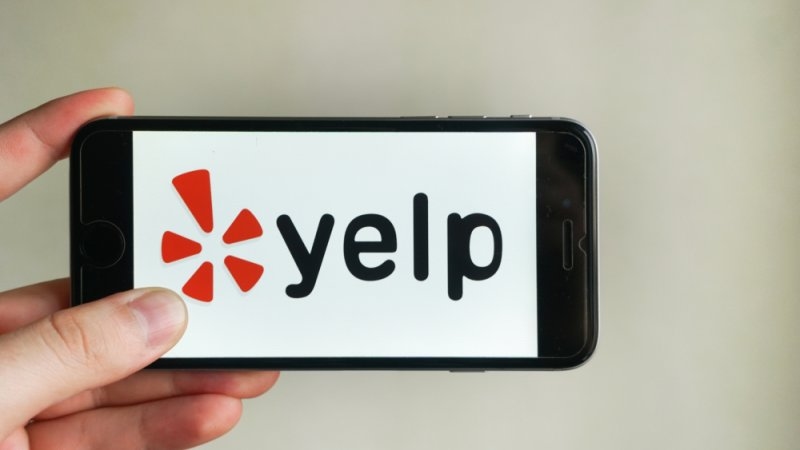 man holding a phone with Yelp application logo on screen