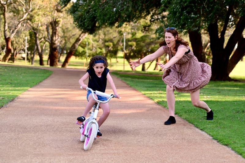 helicopter parent mother saving her kid from falling off a bicycle