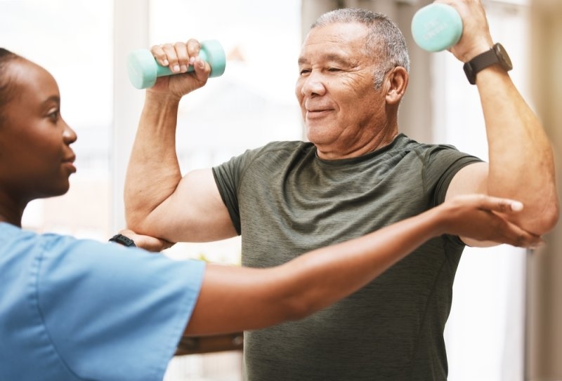 Nurse helping an old man exercise with dumbbells during his recovery