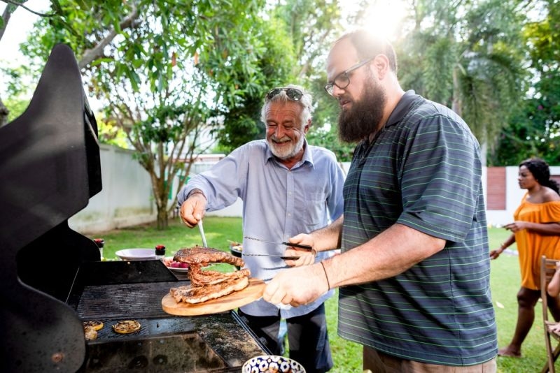 son and father making grilled meat at the backyard
