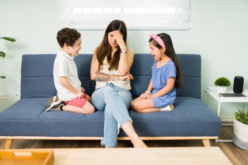 A mother sitting between two children who appear upset or argumentative, suggesting family conflict or parenting stress.