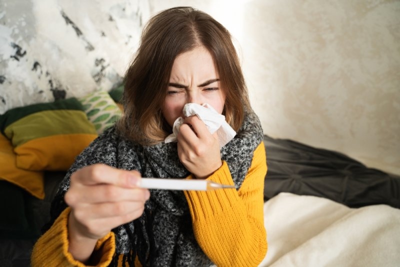 Sick young woman looking at a thermometer suffering from a viral infection.