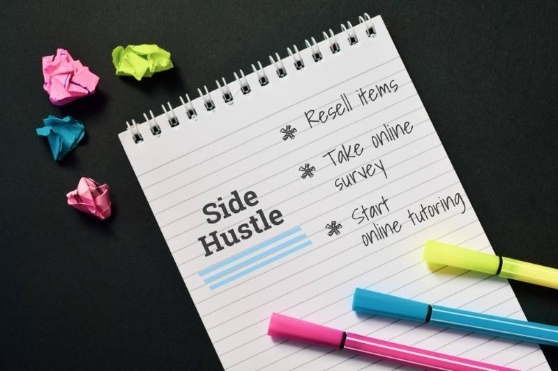 Notebook with ‘Side Hustle’ ideas like reselling items and online tutoring, with colorful pens.