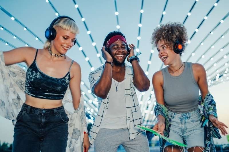 Three young adults wearing headphones and dancing happily under bright lights at a silent disco party.