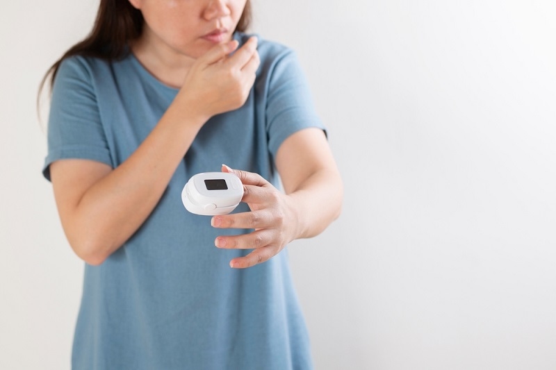 patient having Silent Hypoxia measures blood saturation with an electronic pulse oximeter on her finger.