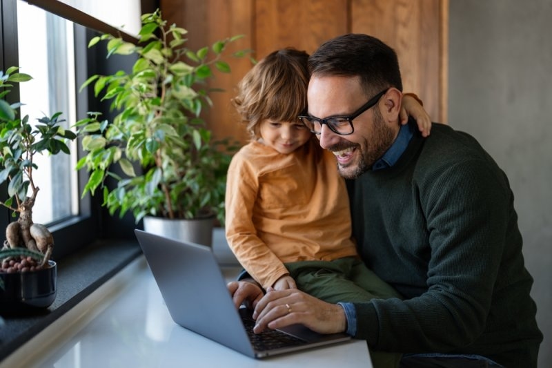 Family portrait of happy young dad and little son relax at home using computer, having fun together