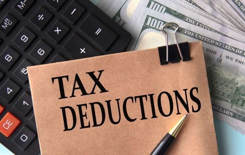 A card labeled “Tax Deductions” is placed beside a calculator, pen, and U.S. dollar bills.