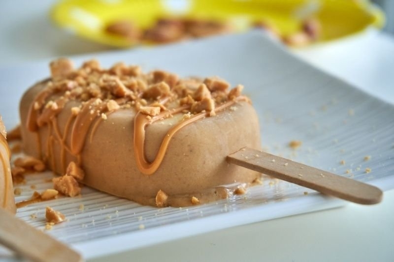 Peanut butter banana popsicles with sprinkles of peanuts and drizzle of raw peanut butter on top, close up.