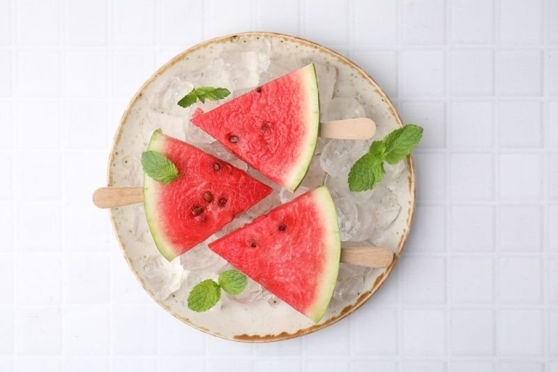 Pieces of tasty watermelon, ice cubes and mint on white tiled table, top view.