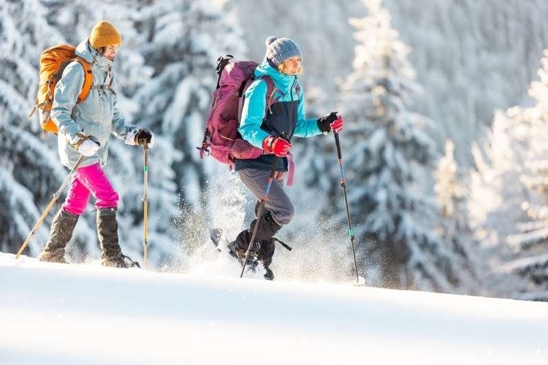 Two women walk in snowshoes in the snow.