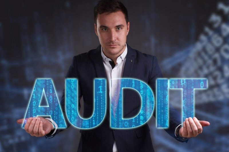 Business professional holding large digital letters spelling “AUDIT,”