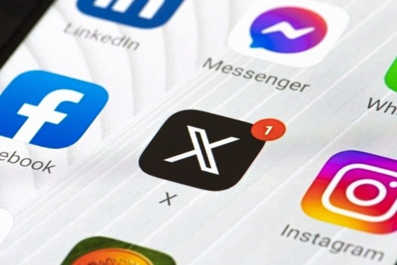 A close-up of a smartphone screen displaying social media app icons, including LinkedIn, Messenger, Facebook, X, and Instagram.