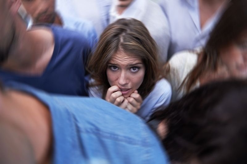 Young woman appearing anxious while standing in a crowded group of people, representing social anxiety, stress, or discomfort in social situations.