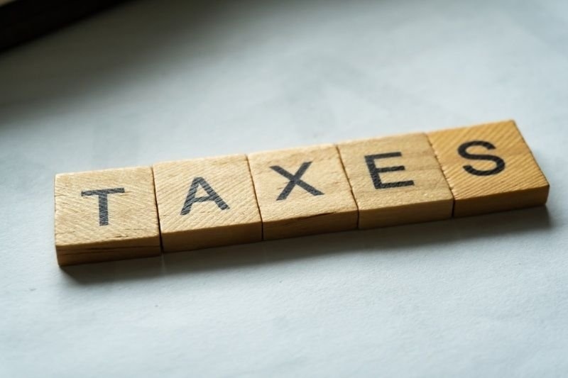 Wooden letter blocks spelling “TAXES” on a light-colored surface.