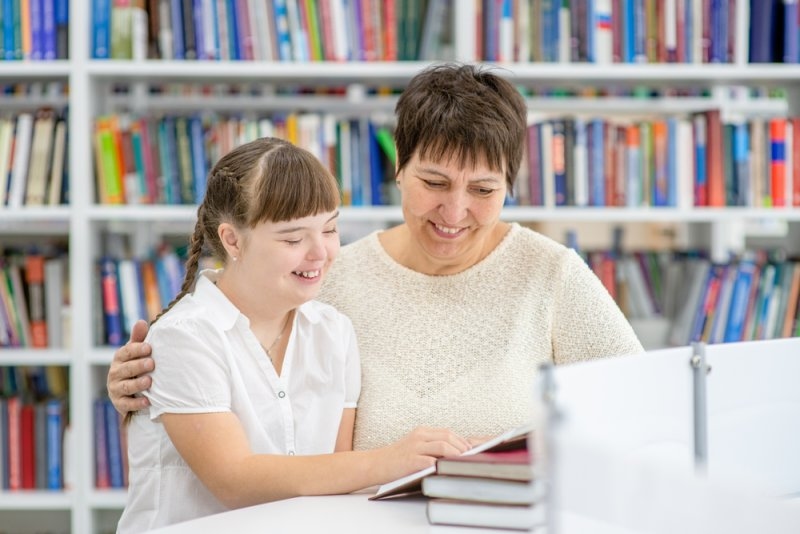 A teacher and student working together with books in a library or classroom.
