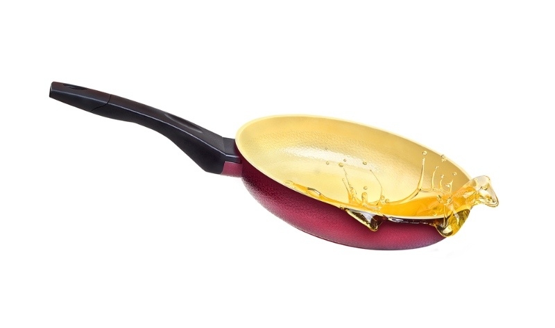 Nonstick frying pan with oil splashing out, illustrating cooking splatter on a white background.