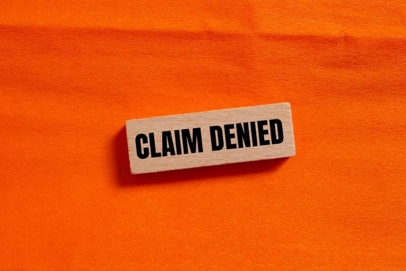 Wooden block displaying the words “Claim Denied” on a bright orange background, symbolizing a rejected insurance or disability benefits claim.