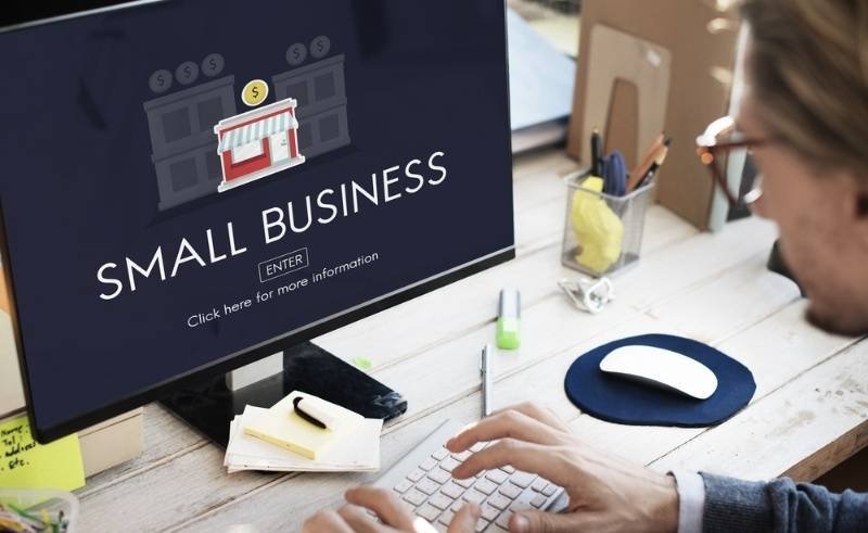 A person working on a desktop computer displaying a small business webpage with a storefront icon and business-related graphics.