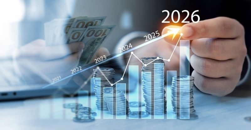 Financial growth concept showing rising bar chart, stacked coins, and hand pointing to 2026 with increasing trend line.