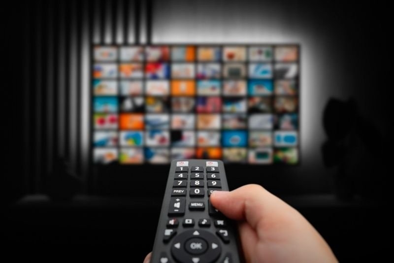 Person using a remote control to browse a television screen filled with streaming content thumbnails.