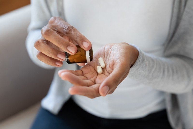 Crop close up of African American woman take pills or tablets from bottle.