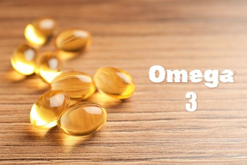 Golden omega-3 supplement capsules arranged on a wooden surface with “Omega 3” text.