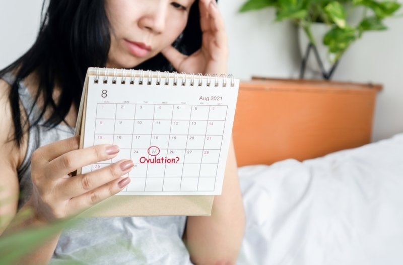 stressed Asian woman looking at calendar waiting for ovulation day
