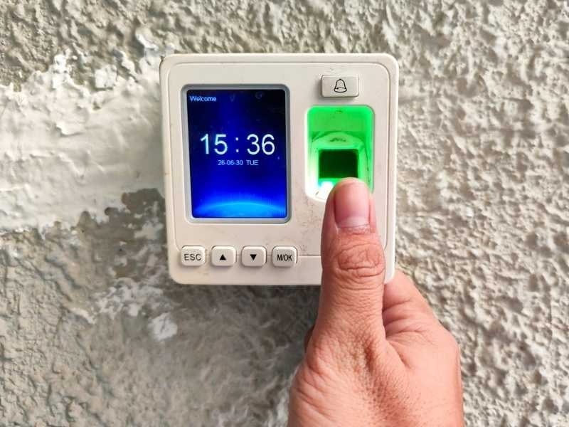 Close-up of a person placing a thumb on a biometric fingerprint scanner for secure employee attendance tracking and access control.