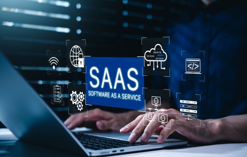 Person using a laptop with a digital “SAAS Software as a Service” interface surrounded by cloud computing, security, connectivity, and technology icons.