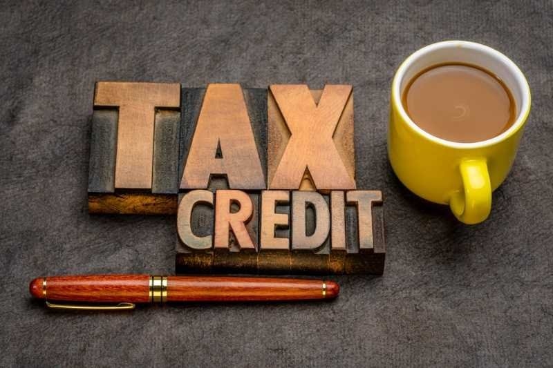 Wooden letter blocks spelling "Tax Credit" beside a coffee cup and pen.