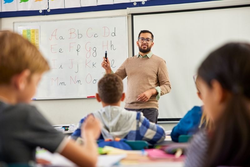 male teacher helping students learn english alphabets