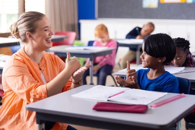 Using sign language, female teacher and boy engaging in communication at school.