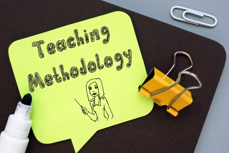 A bright green note displaying “Teaching Methodology” with a hand-drawn illustration of a teacher, surrounded by stationery and paper clips.