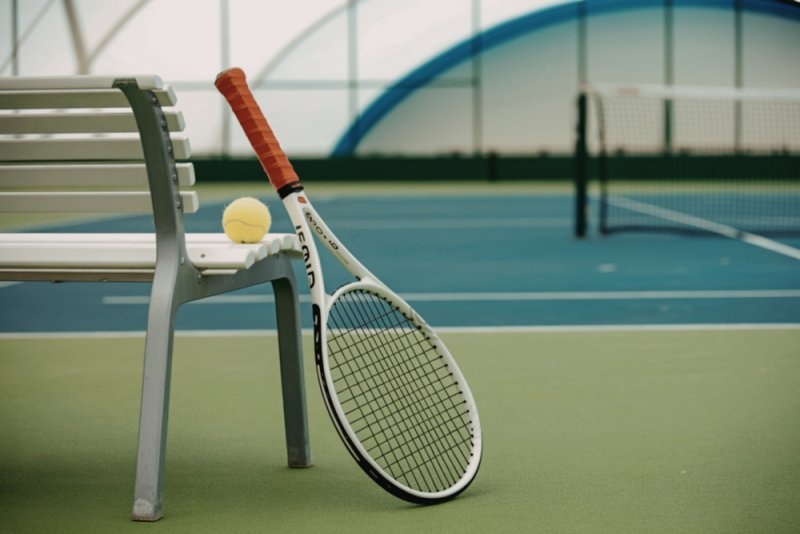 tennis racket with an orange grip and a bright yellow ball