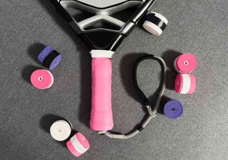 Tennis racket with colorful grip tapes and accessories on a gray surface.