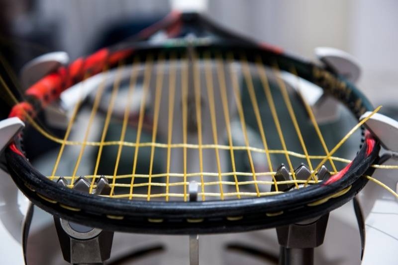 Close-up of a tennis racket being restrung with yellow strings.