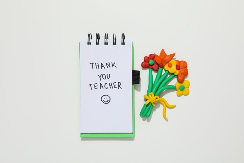 A handwritten “Thank You Teacher” note displayed beside a handmade flower bouquet.