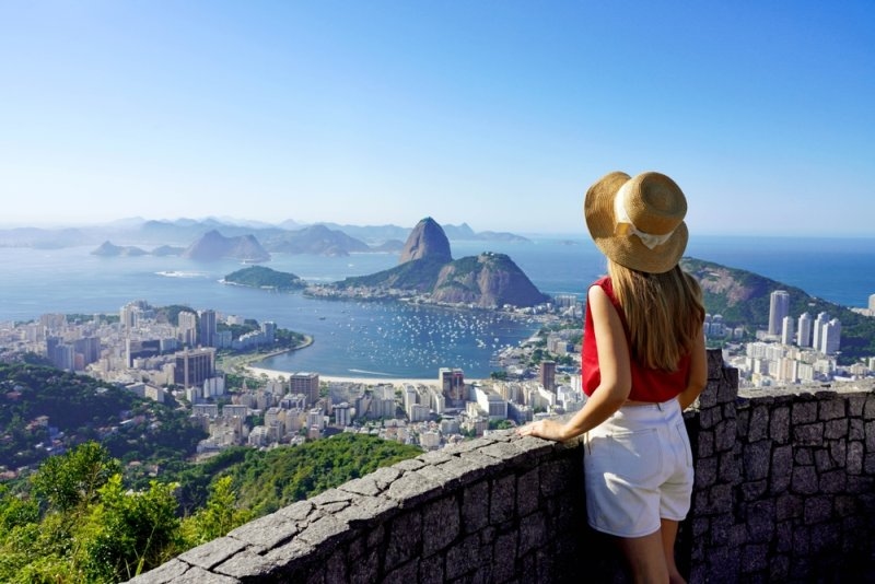 Traveler overlooking Rio de Janeiro from a viewpoint, with Sugarloaf Mountain, Guanabara Bay, and the city visible below.
