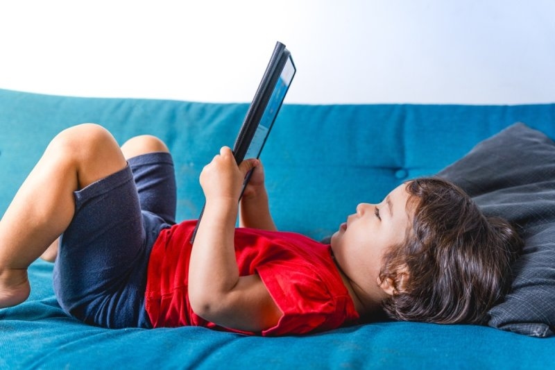 Young child relaxing on a couch while using a tablet.