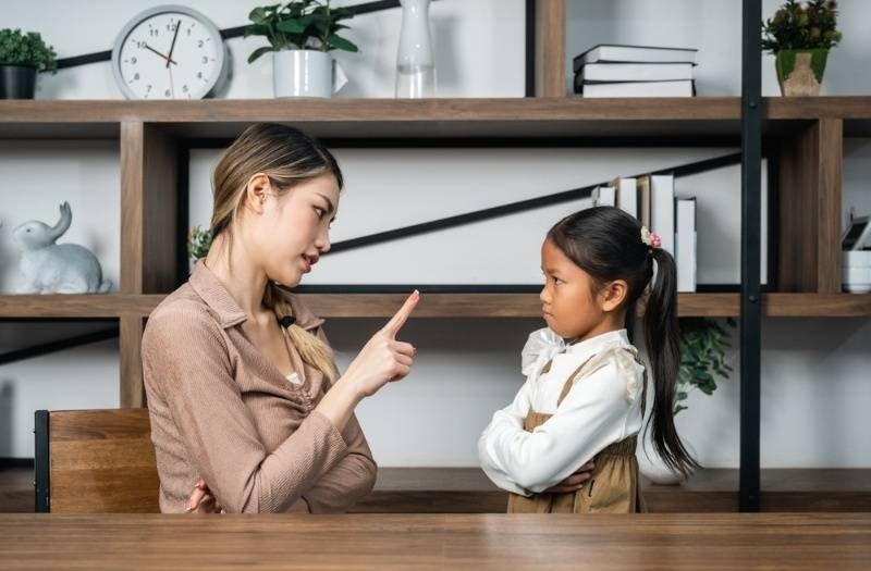 Parent pointing a finger while talking to a young child with crossed arms.