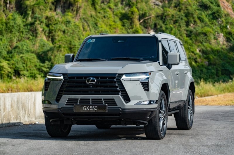 White Lexus GX 550 SUV parked on a paved road surrounded by green hills.