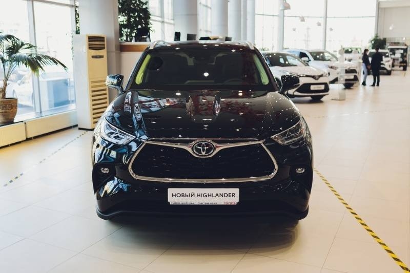 A black Toyota Highlander is displayed prominently inside a bright car dealership showroom.