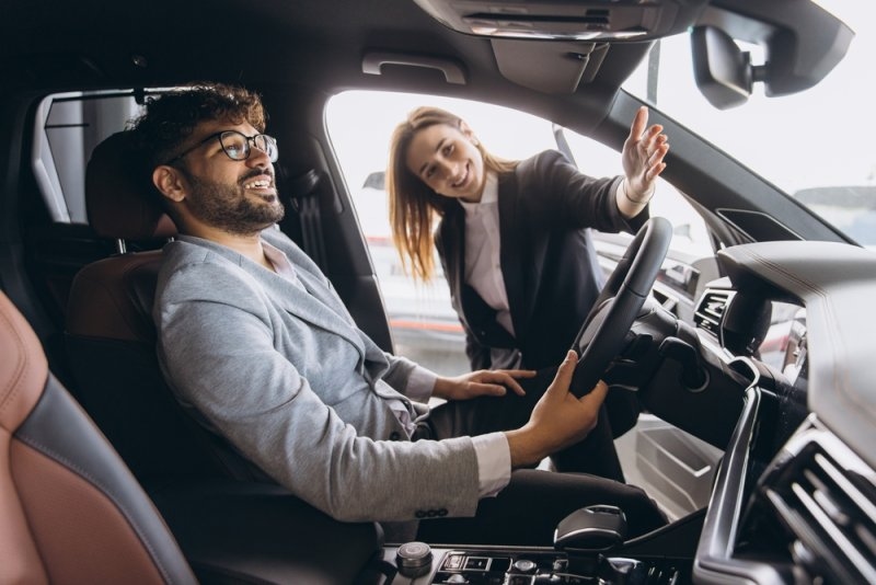 A salesperson explains vehicle features to a customer seated inside a modern SUV.