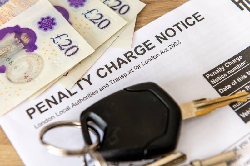 Penalty charge notice document with car keys and British currency notes on a wooden surface.
