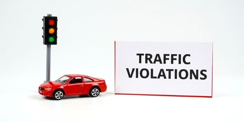 Toy red car next to a traffic light and a sign reading ‘Traffic Violations’ on a white background.
